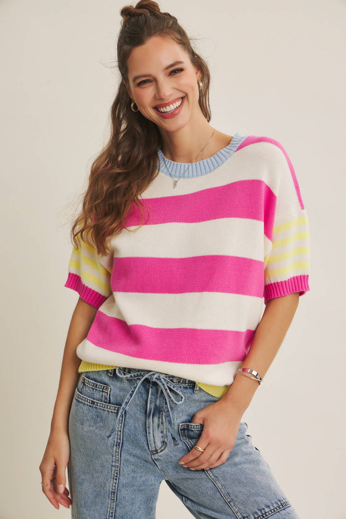 Woman wearing a pink white striped sweater and jeans on a plain background