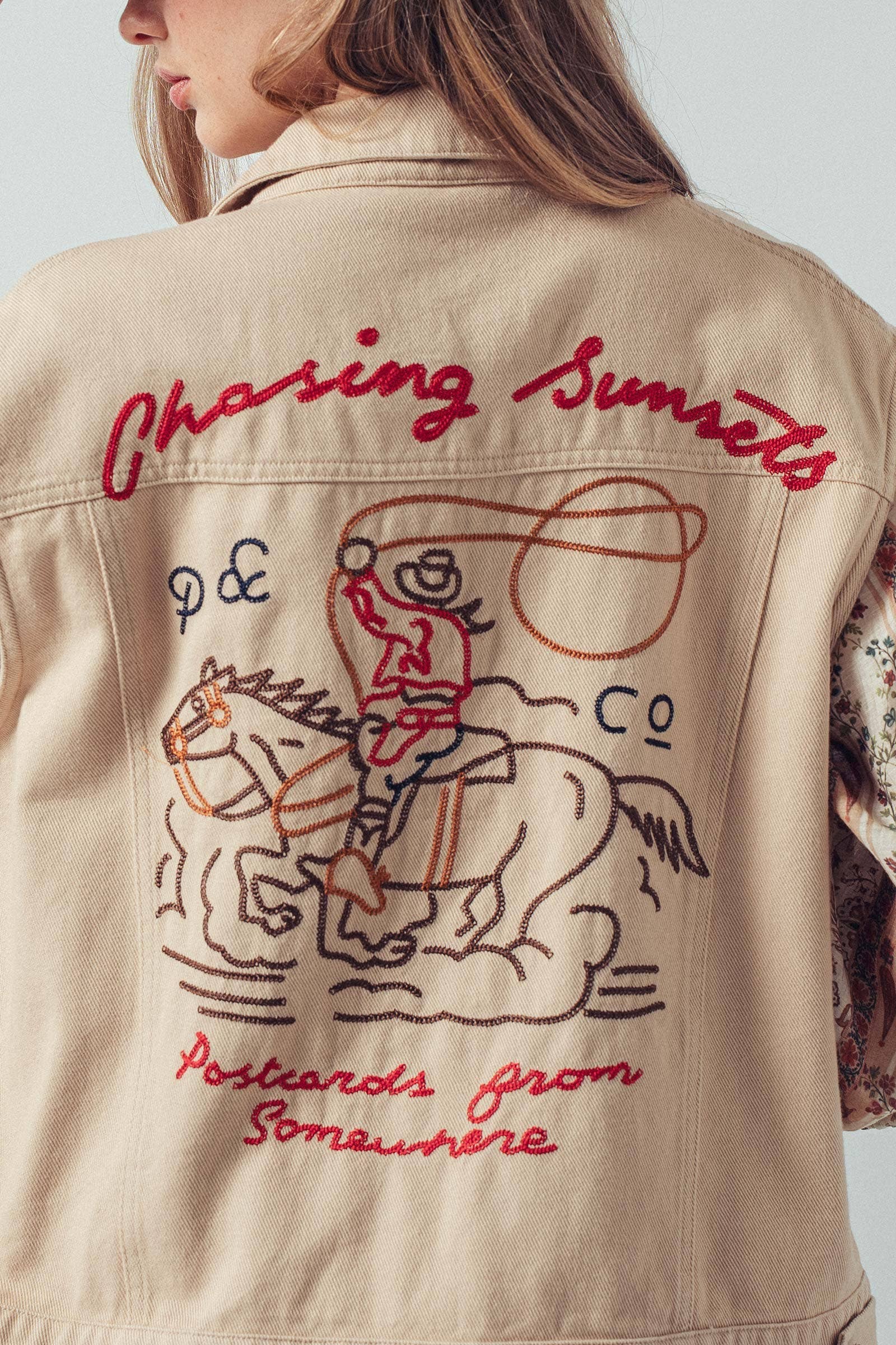 Beige jacket with embroidered design and text on a plain background