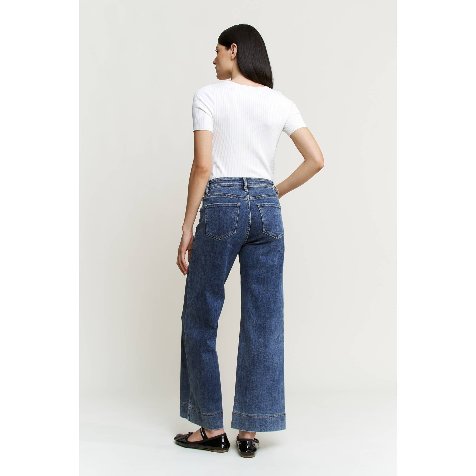 Person wearing blue jeans and a white t-shirt on a plain background showing back view.