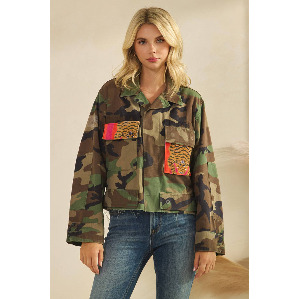 Woman wearing a camouflage jacket with colorful patches on a plain background. Front view.