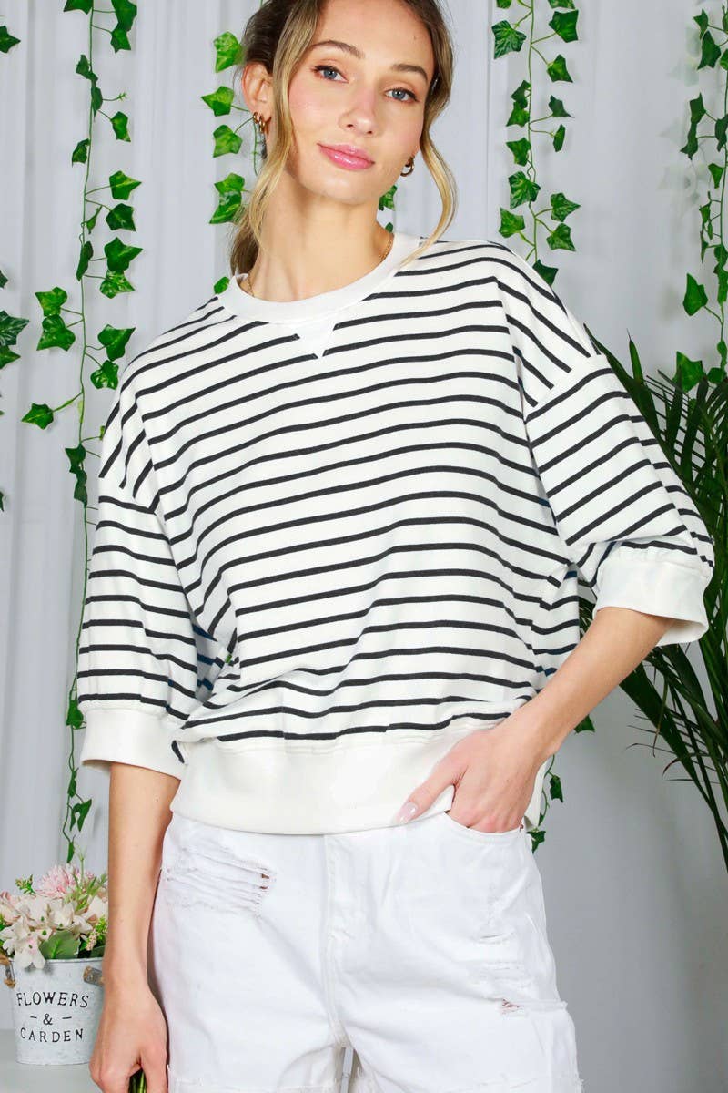 Woman wearing a black and white striped sweater with a white background and greenery.
