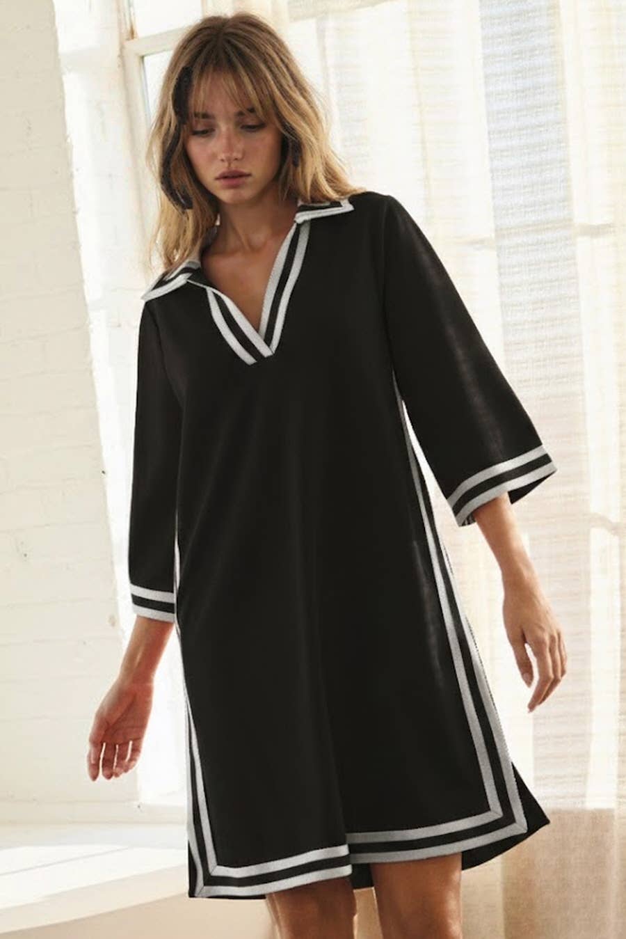 Woman wearing a black dress with white trim in a bright room.