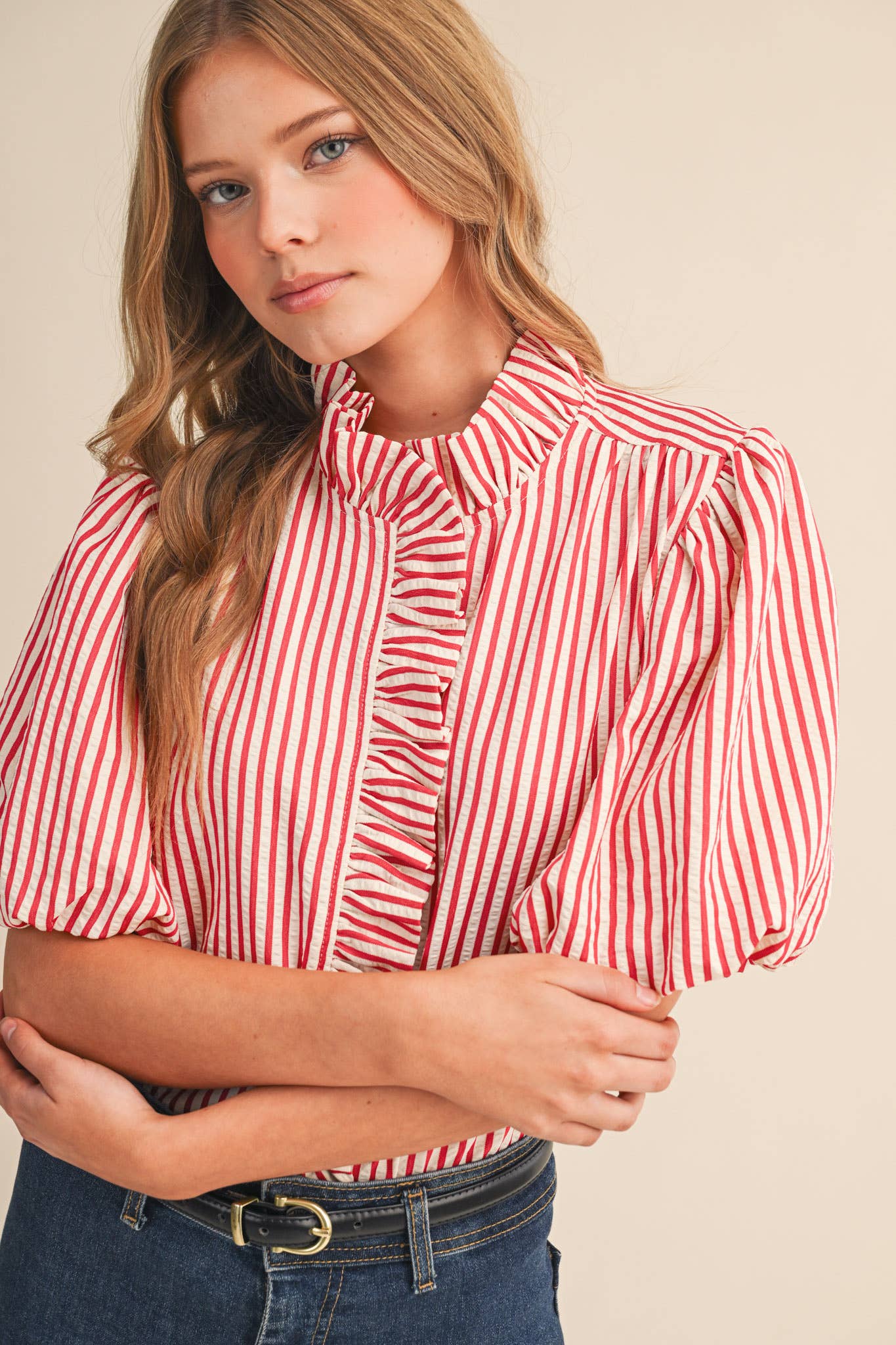 Woman wearing a red and white striped blouse with puffed sleeves on a beige background