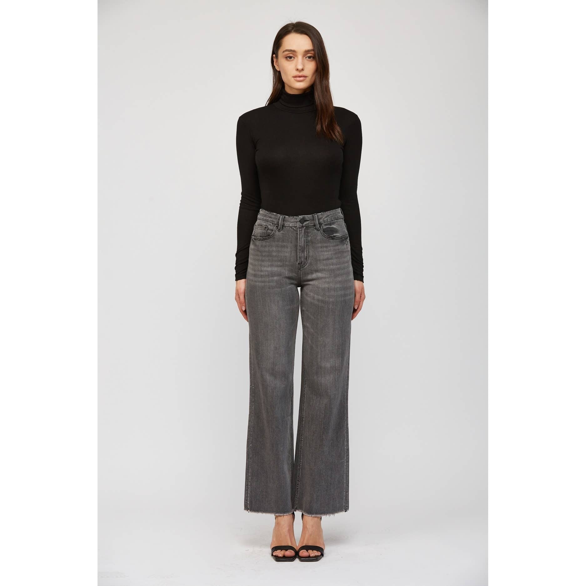 Woman wearing a black turtleneck and gray wide-leg jeans on a white background