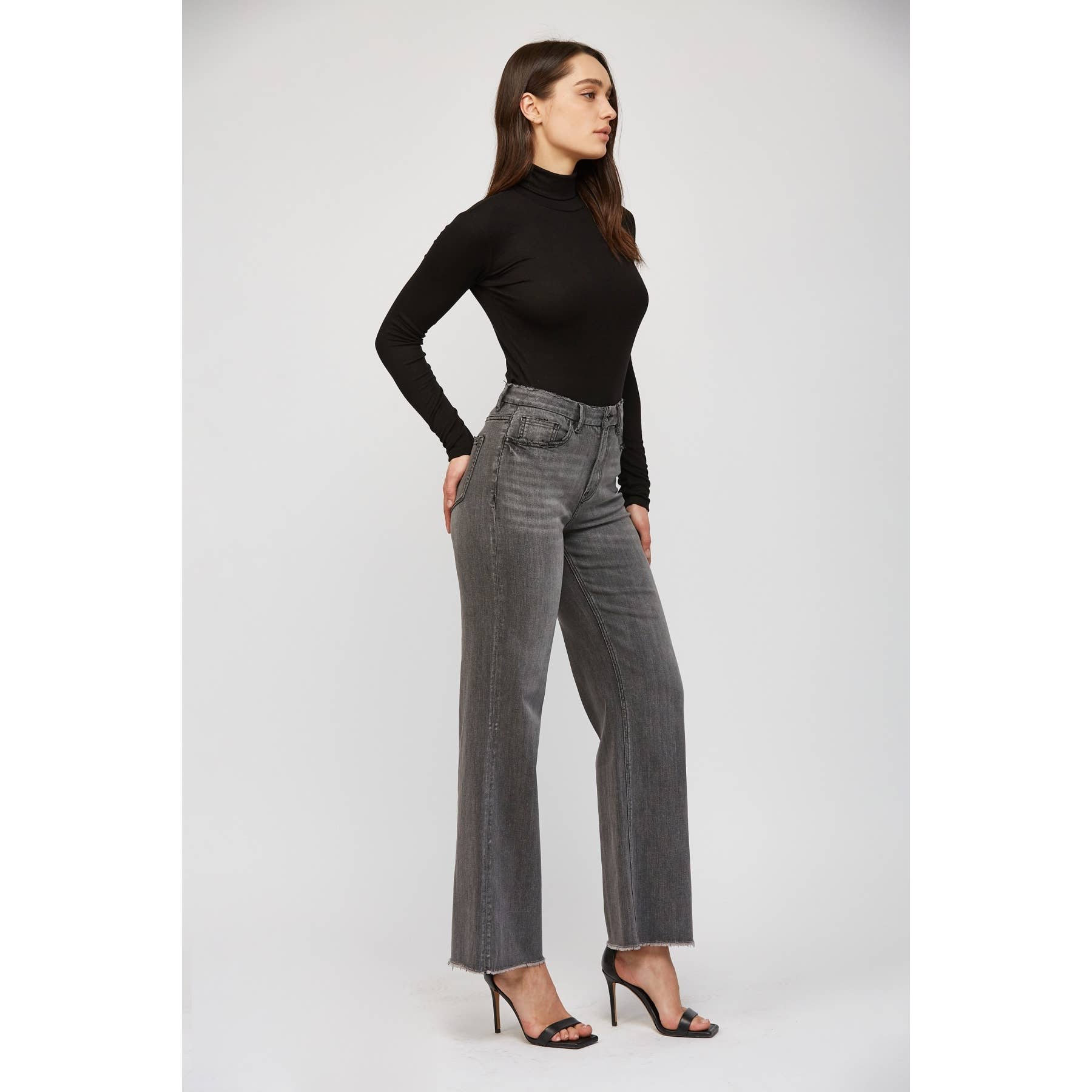 Woman wearing a black long-sleeve top and gray flared jeans on a white background. Showing side view.