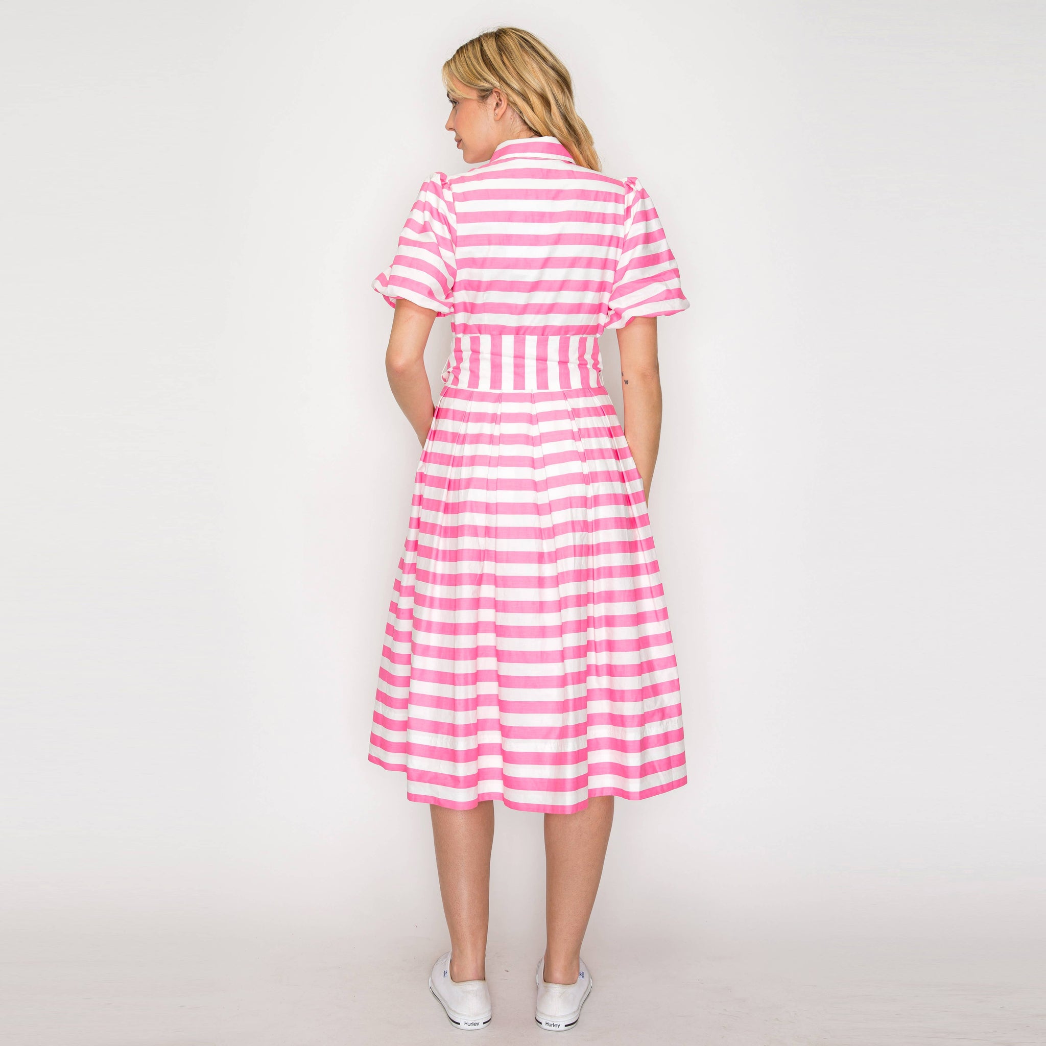 Woman wearing a pink and white striped dress on a plain background. Back view.