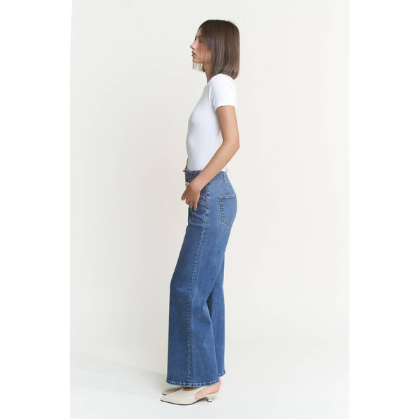 Woman wearing blue jeans and a white shirt on a plain background showing the side view