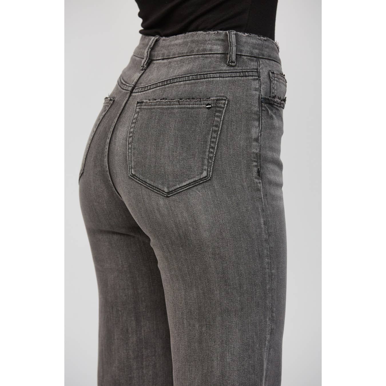 Gray jeans on a plain background zoomed in on pockets and back yoke.