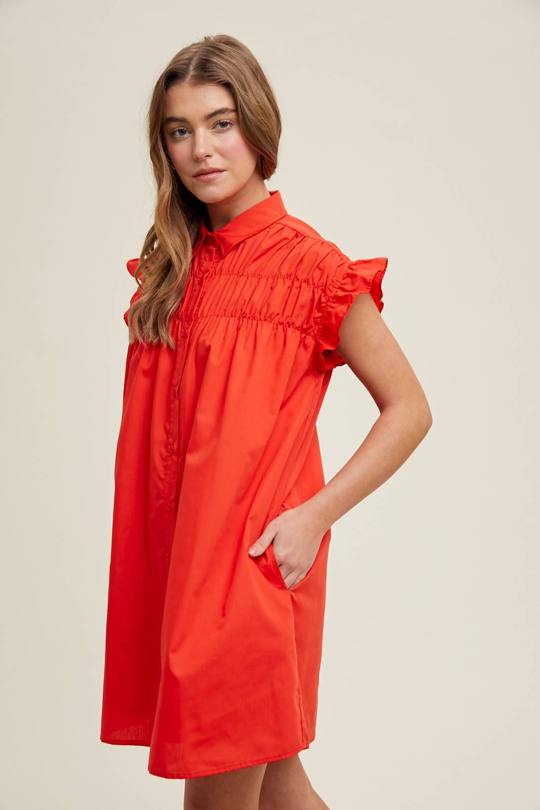 Woman wearing a red dress against a beige background showing side view.