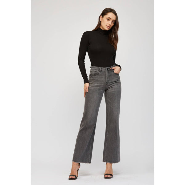 Woman wearing a black turtleneck and gray flared jeans on a white background
