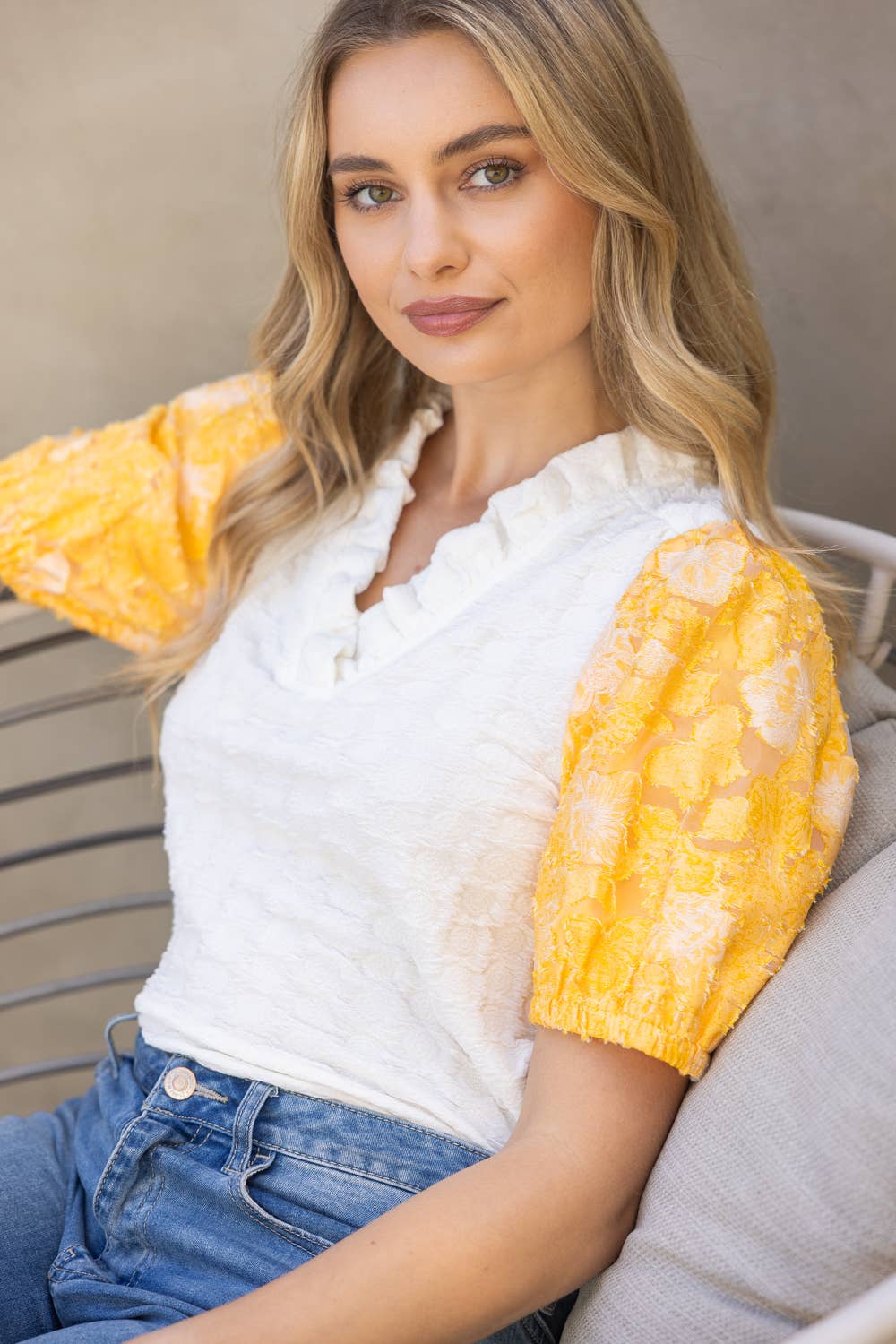 Woman wearing a white top with yellow sleeves sitting on a chair.