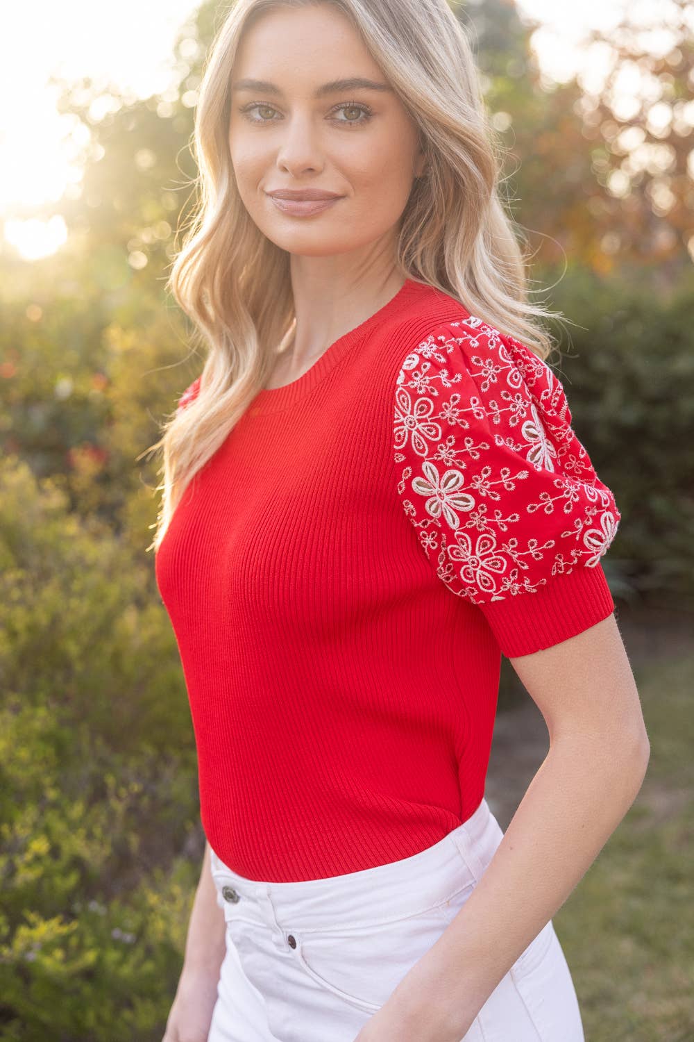 Woman wearing a red top with white floral patterns on the sleeves, standing outdoors.
