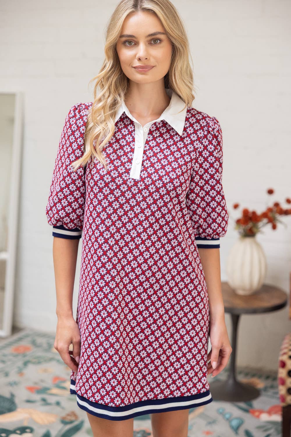 Woman wearing a red and white patterned dress with a collar in a room setting.