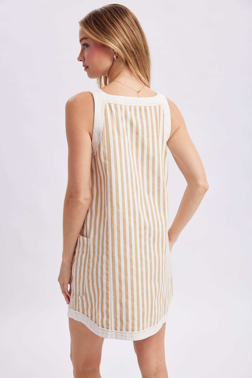Woman wearing a sleeveless, striped dress with a white background showing back view.