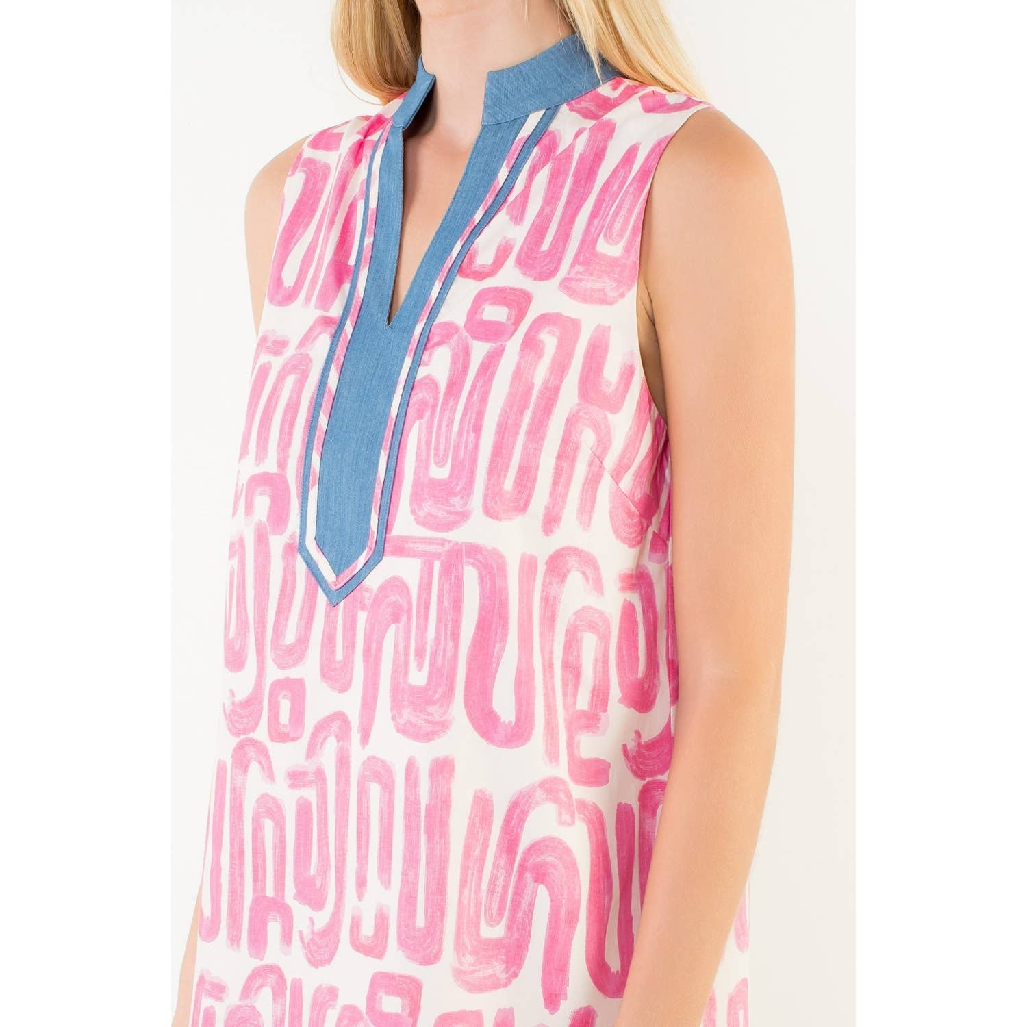 Woman wearing a sleeveless dress with pink abstract pattern and blue neckline on a white background