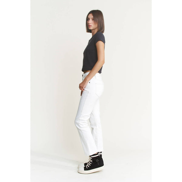 Woman wearing a black top and white pants with black high-top sneakers on a plain background showing side view