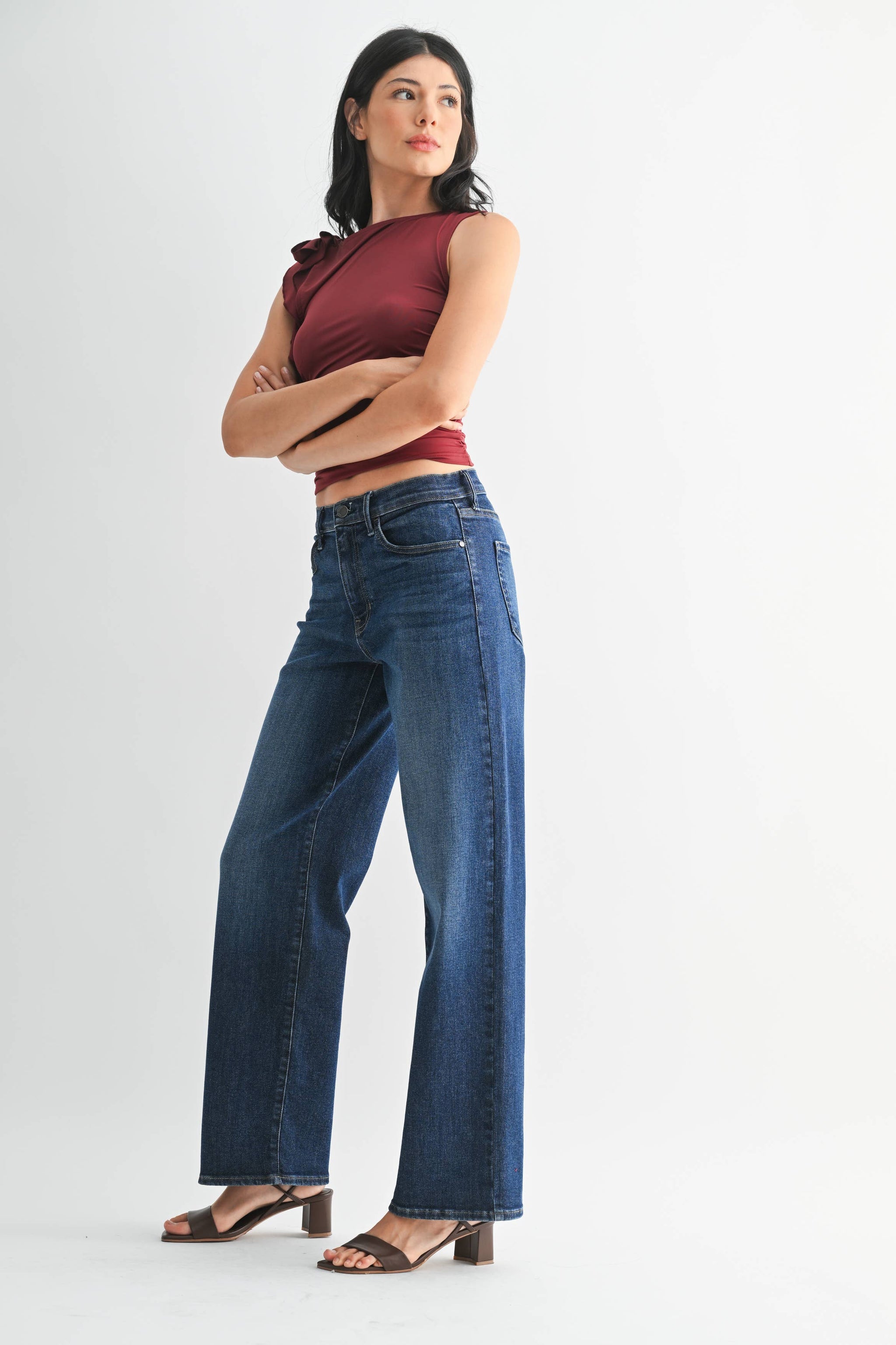 Woman wearing a burgundy top and blue jeans on a white background. Side view with brown short heels.