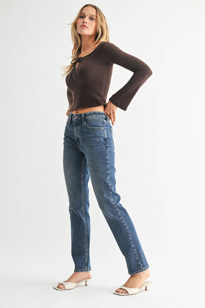 Woman wearing a brown long-sleeve top and blue jeans on a white background with white kitten heels.  Side View.
