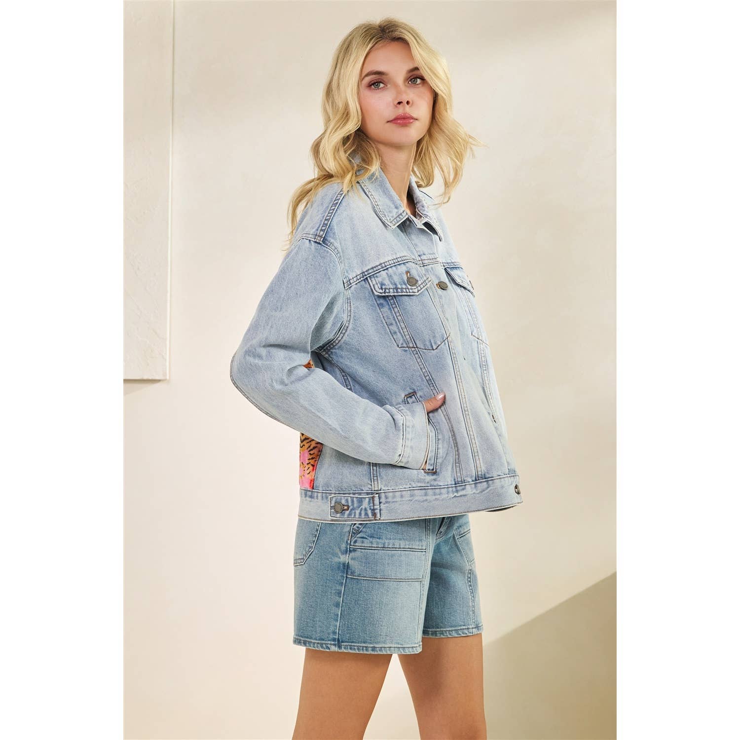 Woman wearing a light blue denim jacket and shorts on a beige background