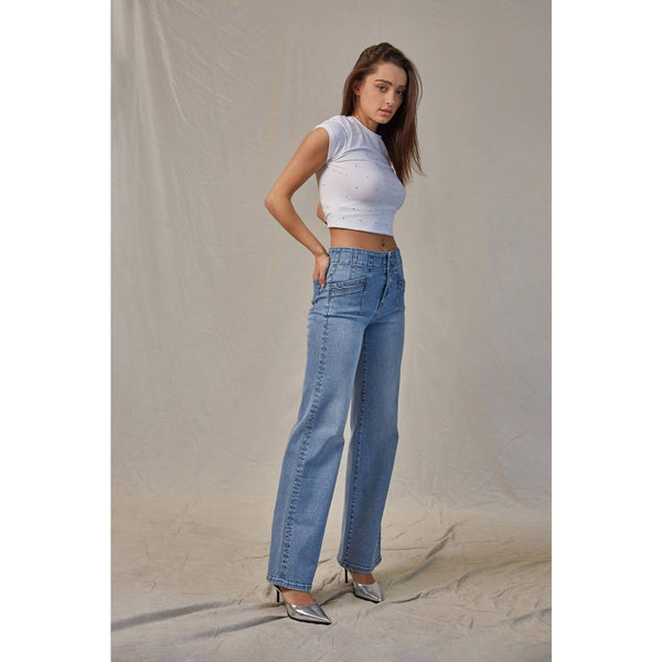 Woman wearing a white crop top and blue jeans against a plain background