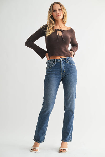 Woman wearing a brown long-sleeve top and blue jeans on a white background