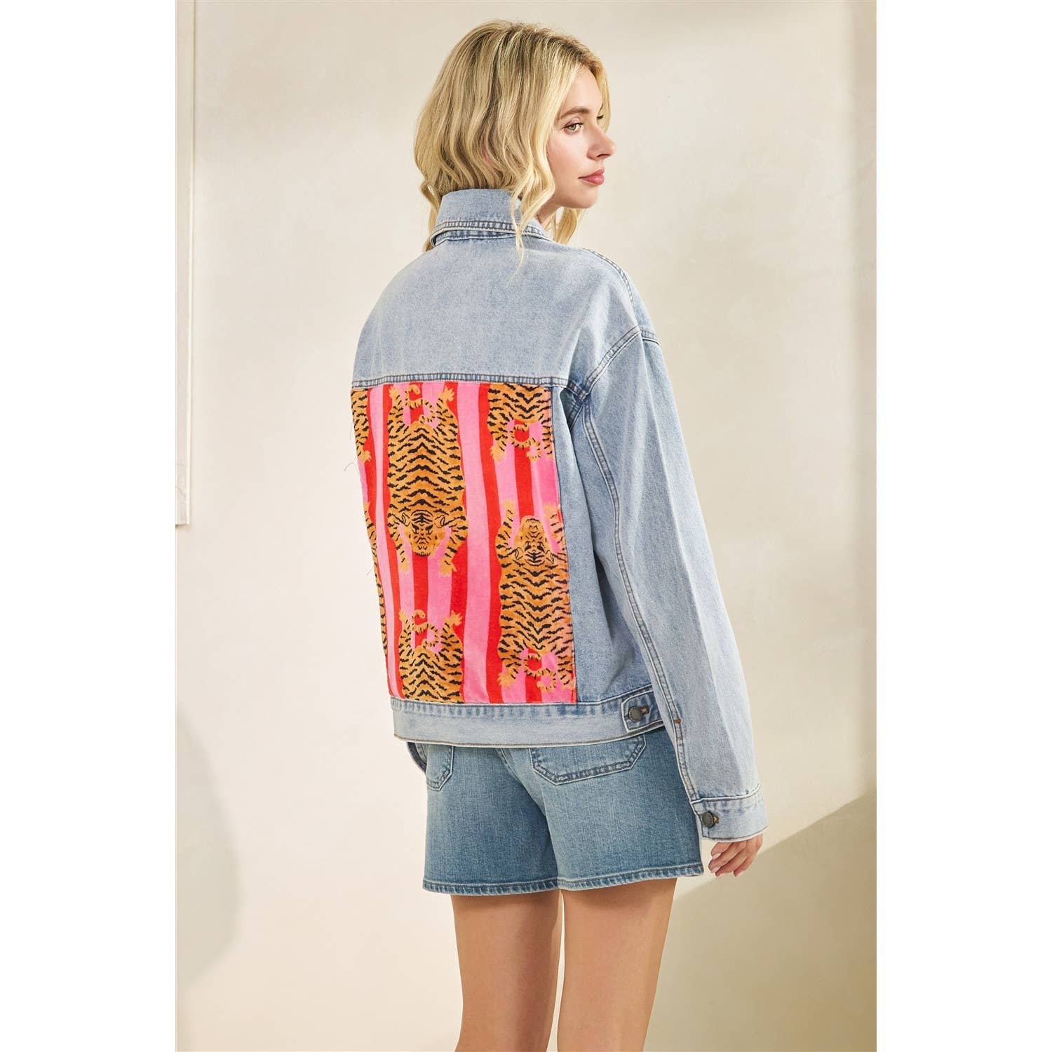 Person wearing a denim jacket with colorful tiger patterned panels on a plain background. Back view.
