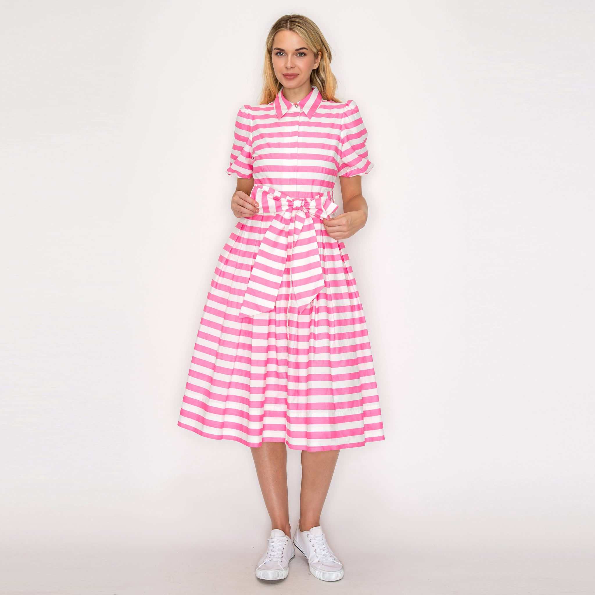 Woman wearing a pink and white striped dress on a plain background
with white sneakers.