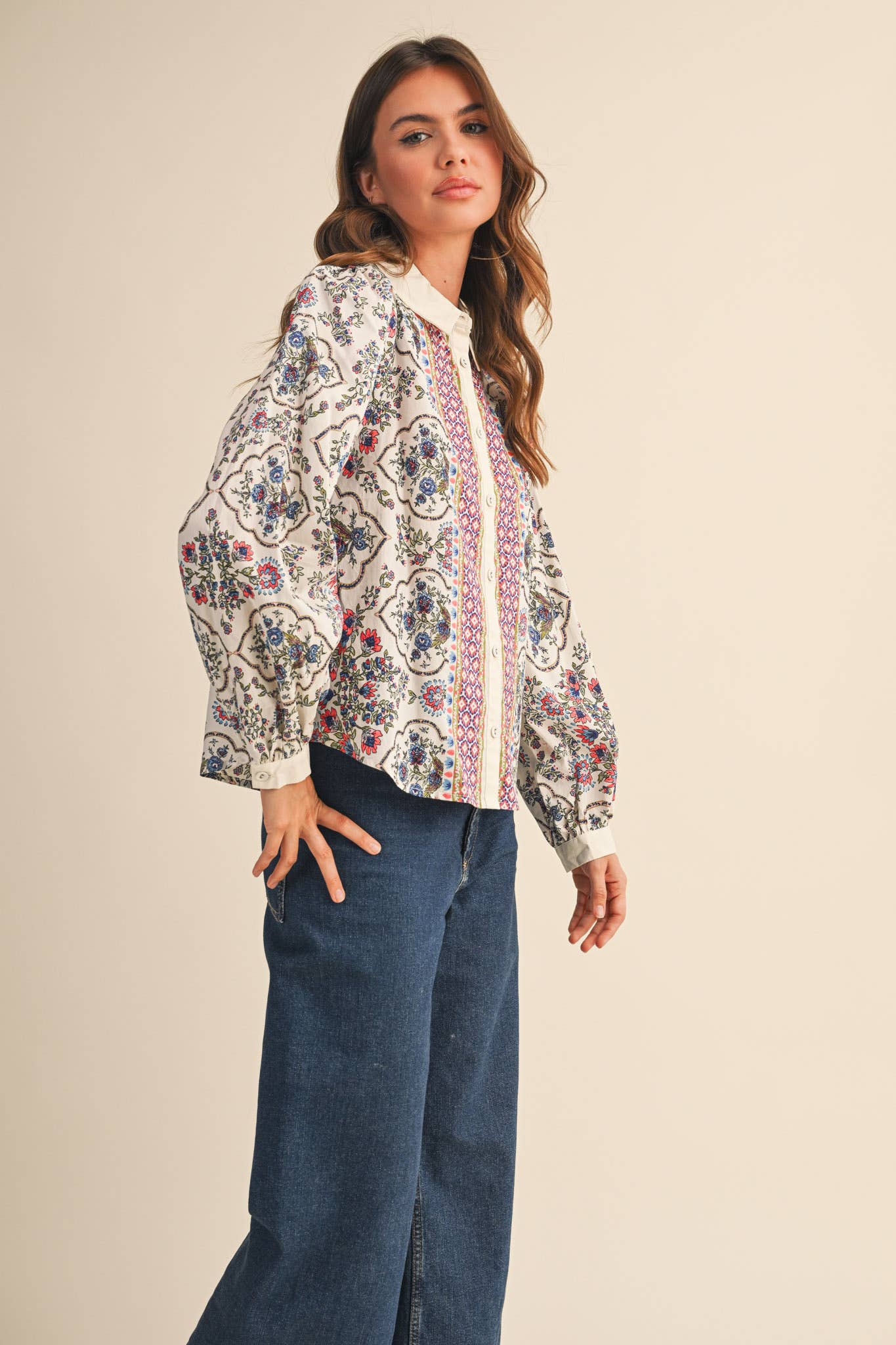 Woman wearing a patterned blouse and blue jeans on a beige background