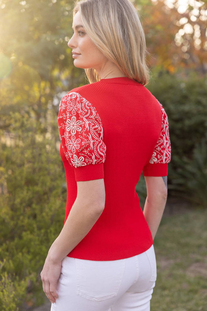 Woman wearing a red top with lace sleeves in an outdoor setting