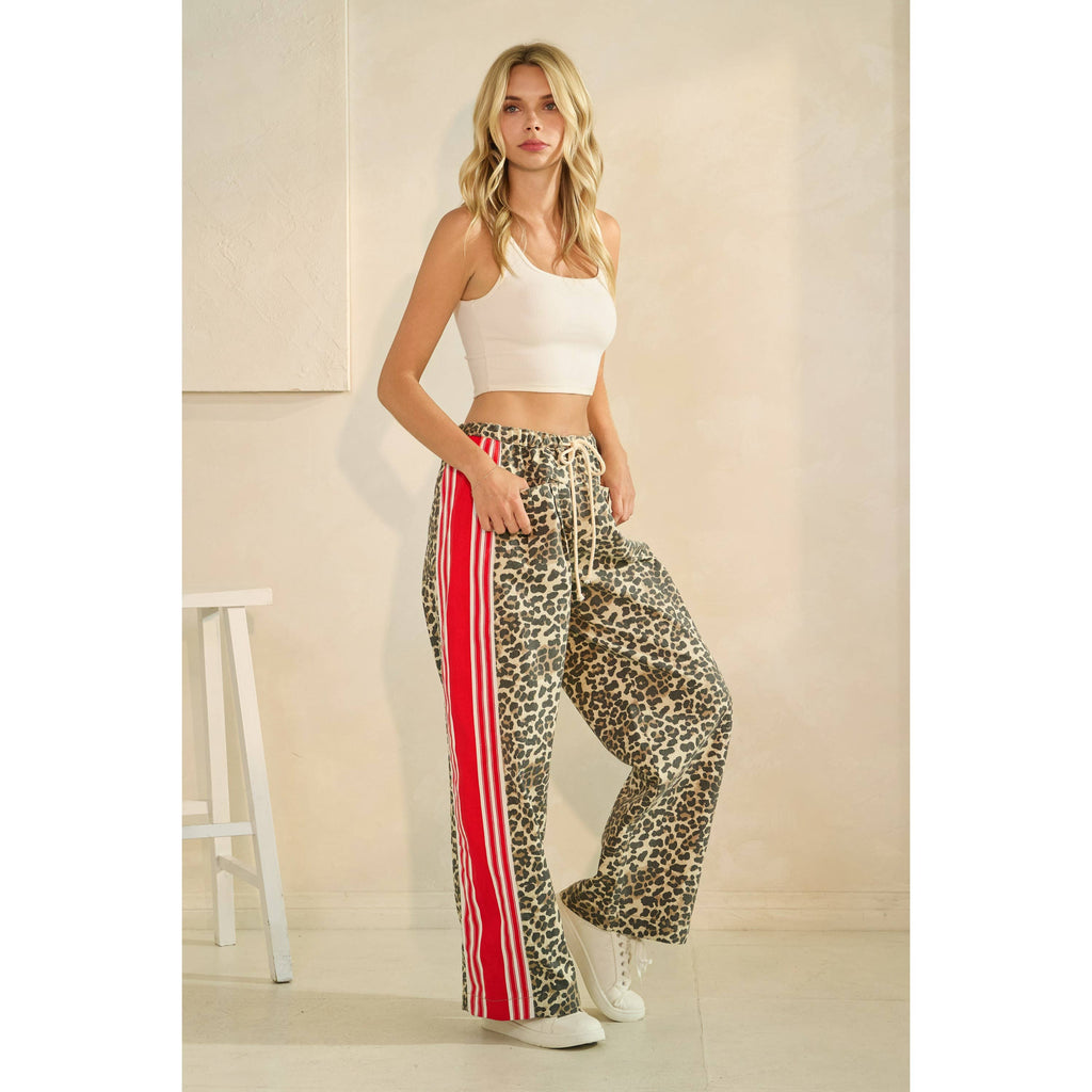 Woman wearing leopard print pants with red stripes and a white top in a minimalistic room. Side view.