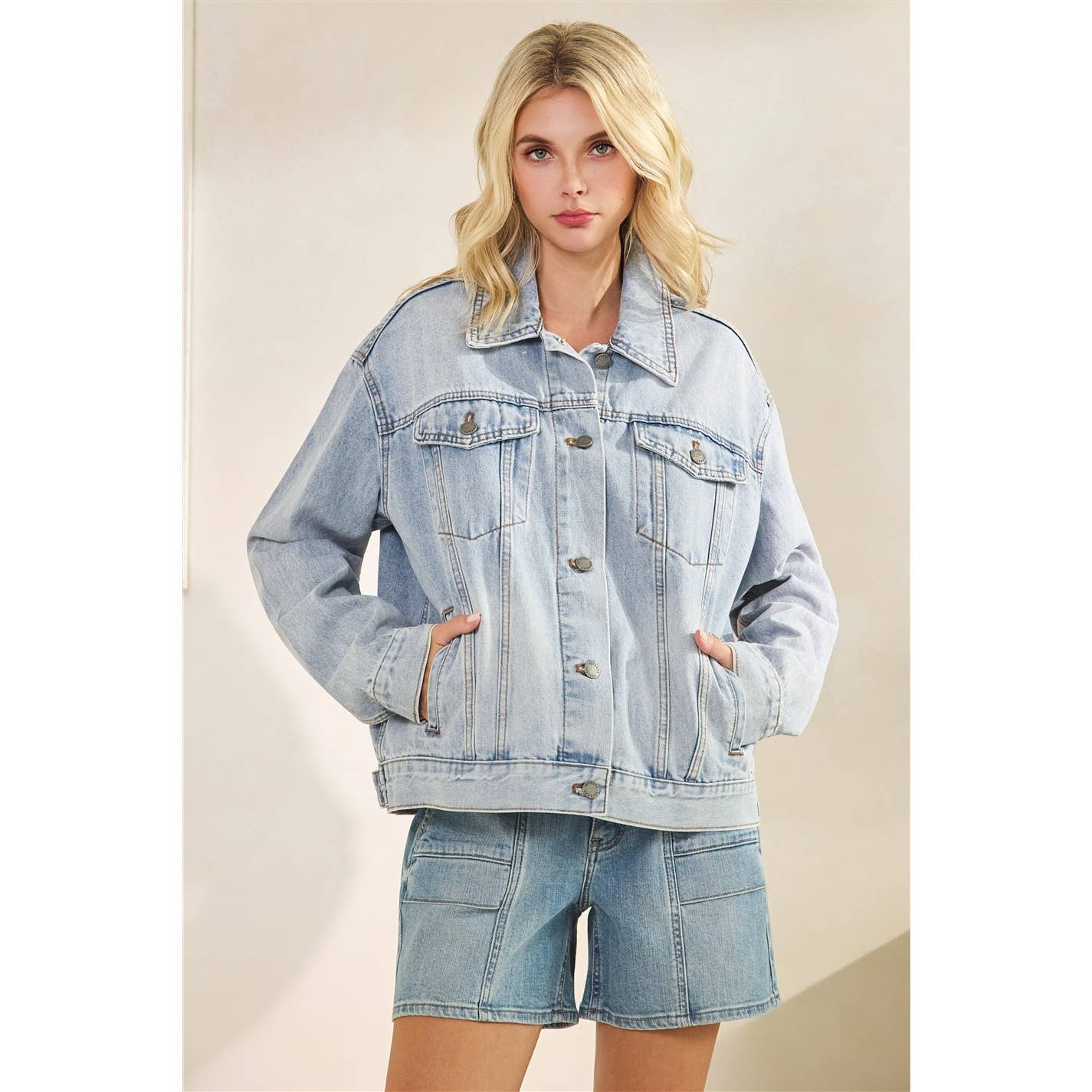 Woman wearing a light blue classic trucker denim jacket and shorts on a grey  background