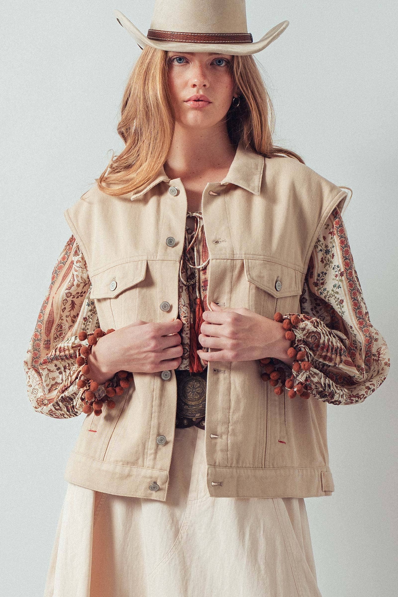 Woman wearing a beige vest over a patterned shirt with a plain background