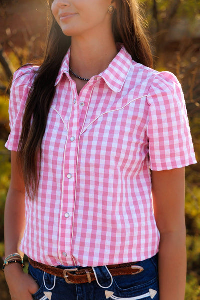 Person wearing a pink and white checkered shirt with a blurred natural background