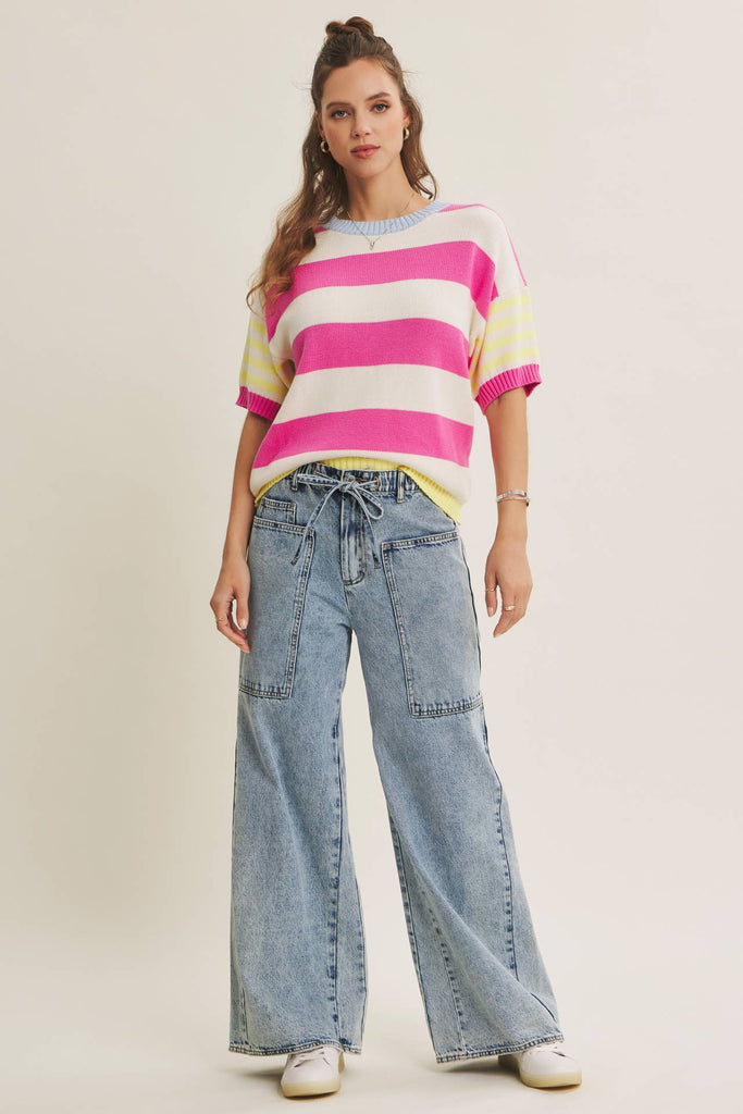 Woman wearing a colorful striped sweater and wide-leg jeans on a plain background