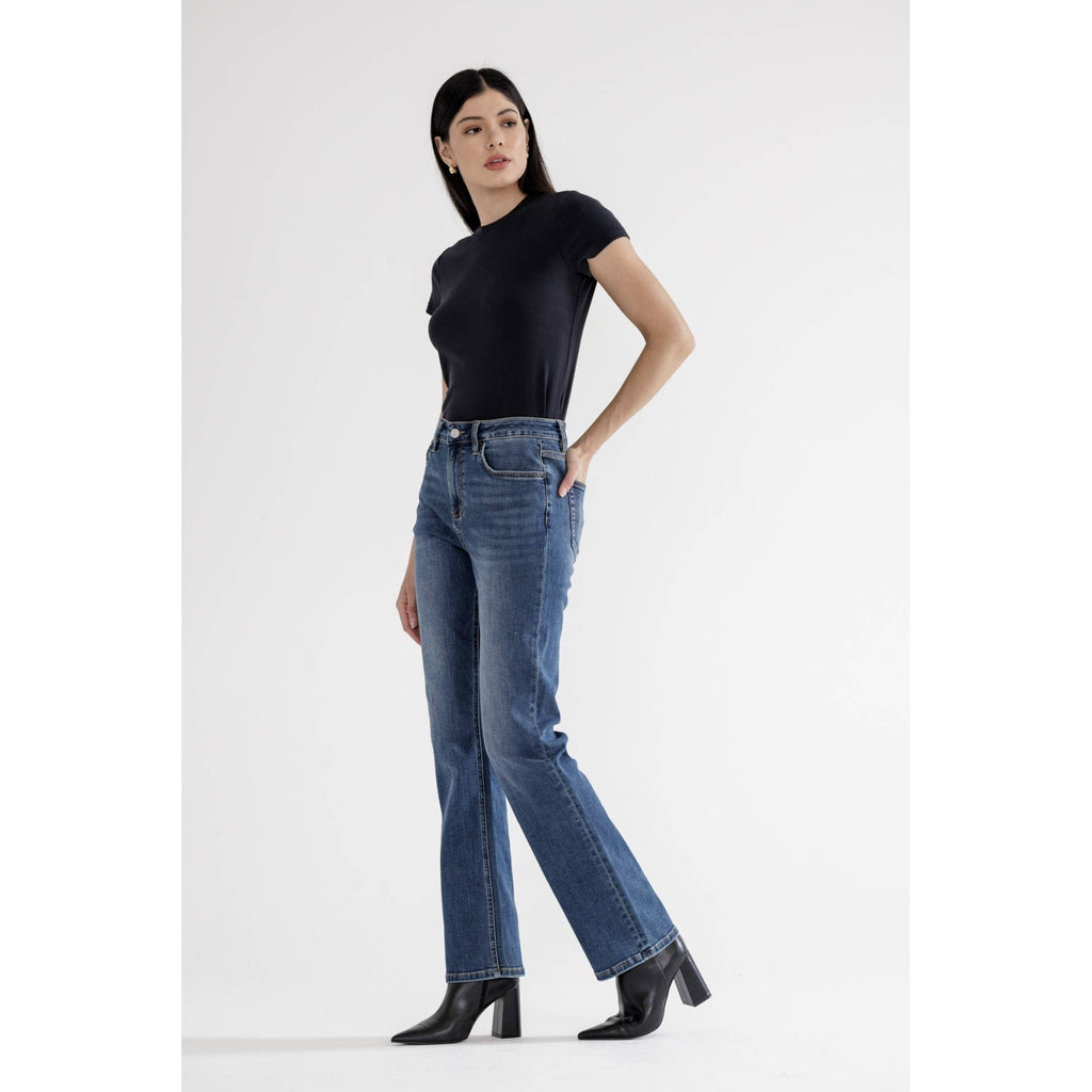 Woman wearing straight full length blue jeans and a black top on a white background showing side view