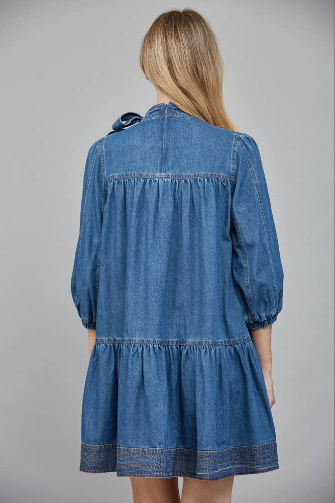 Blue denim dress worn by a person on a gray background showing back view.