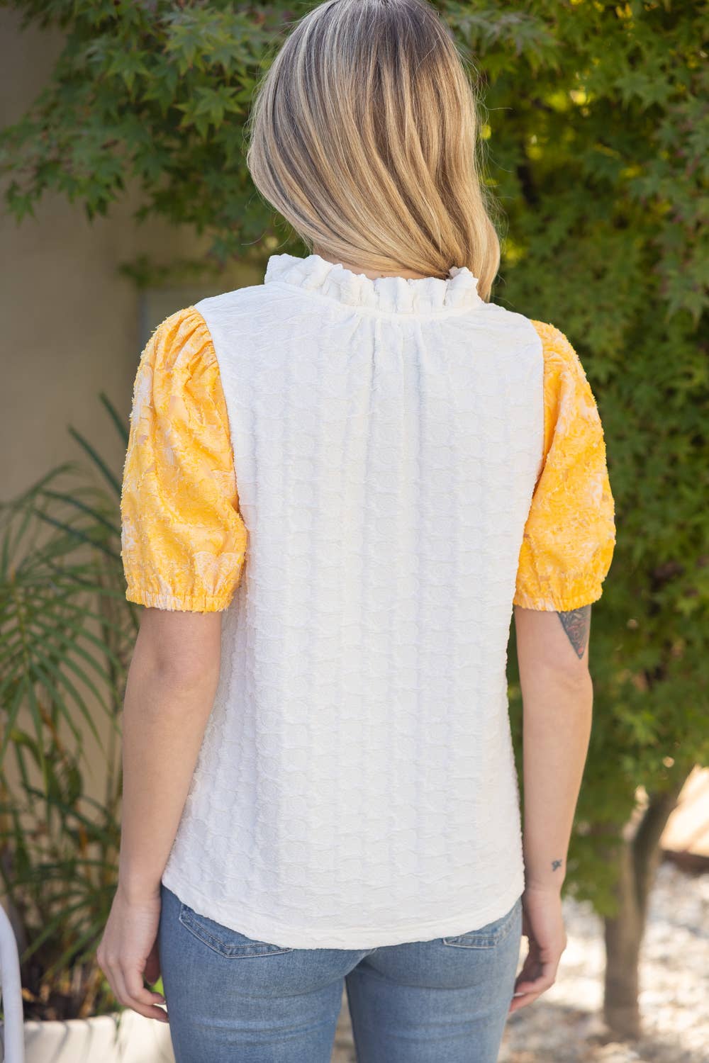 Person wearing a white blouse with yellow sleeves and blue jeans, standing outdoors.