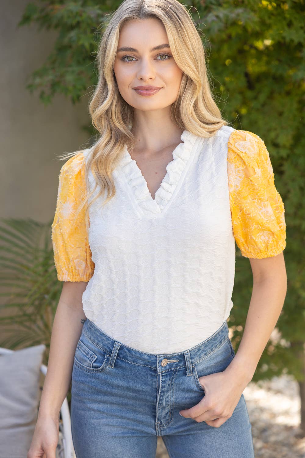 Woman wearing a white top with yellow sleeves and blue jeans outdoors.