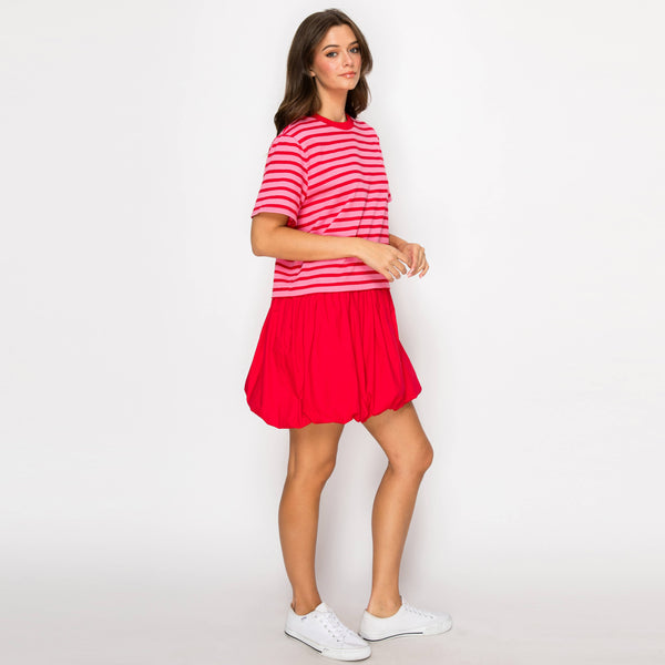 Woman wearing a pink and red striped dress on a white background; side view.