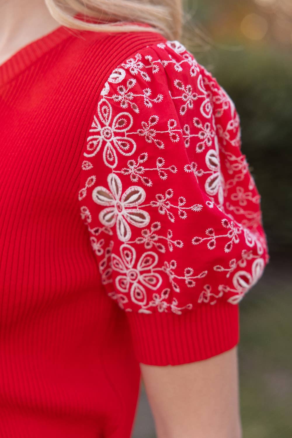Red sweater with white floral patterns on sleeves against a blurred green background