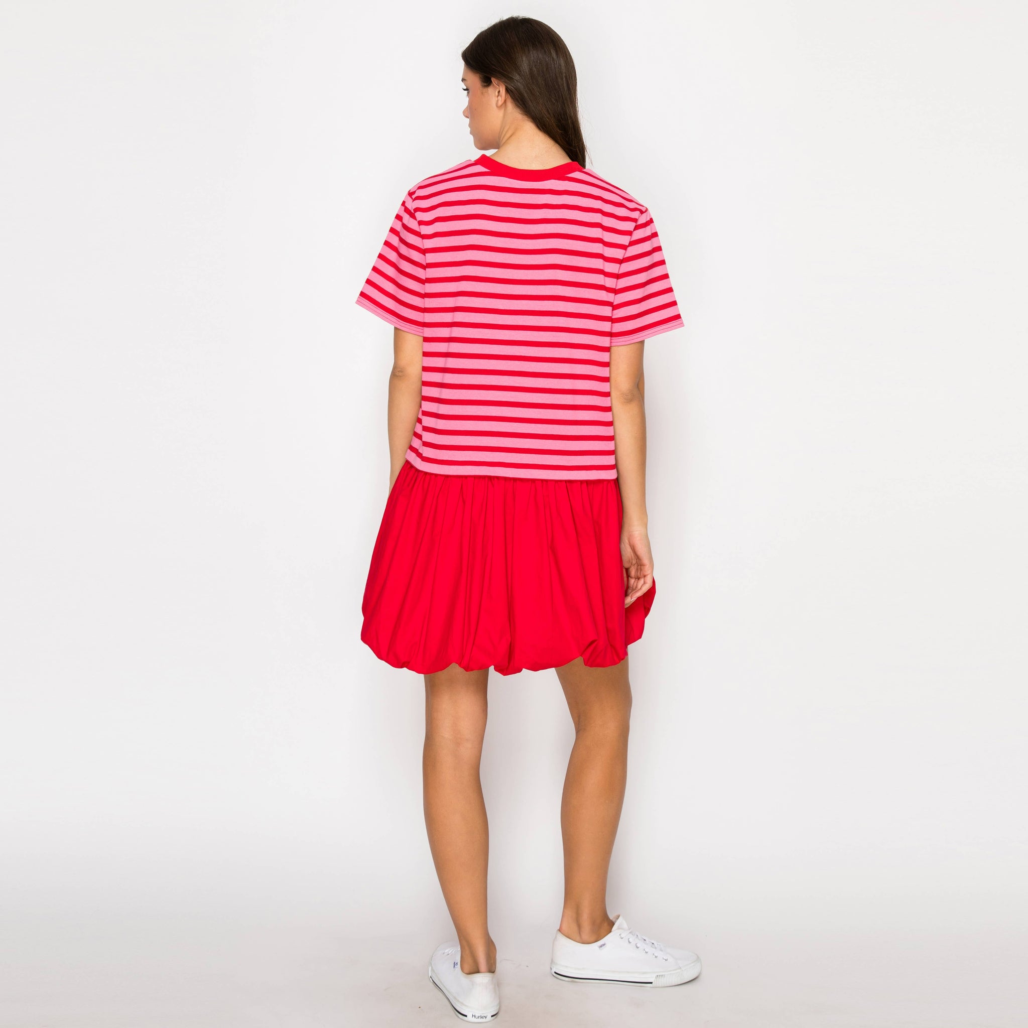 Woman wearing a red and white striped dress with white sneakers showing the back view on a plain background