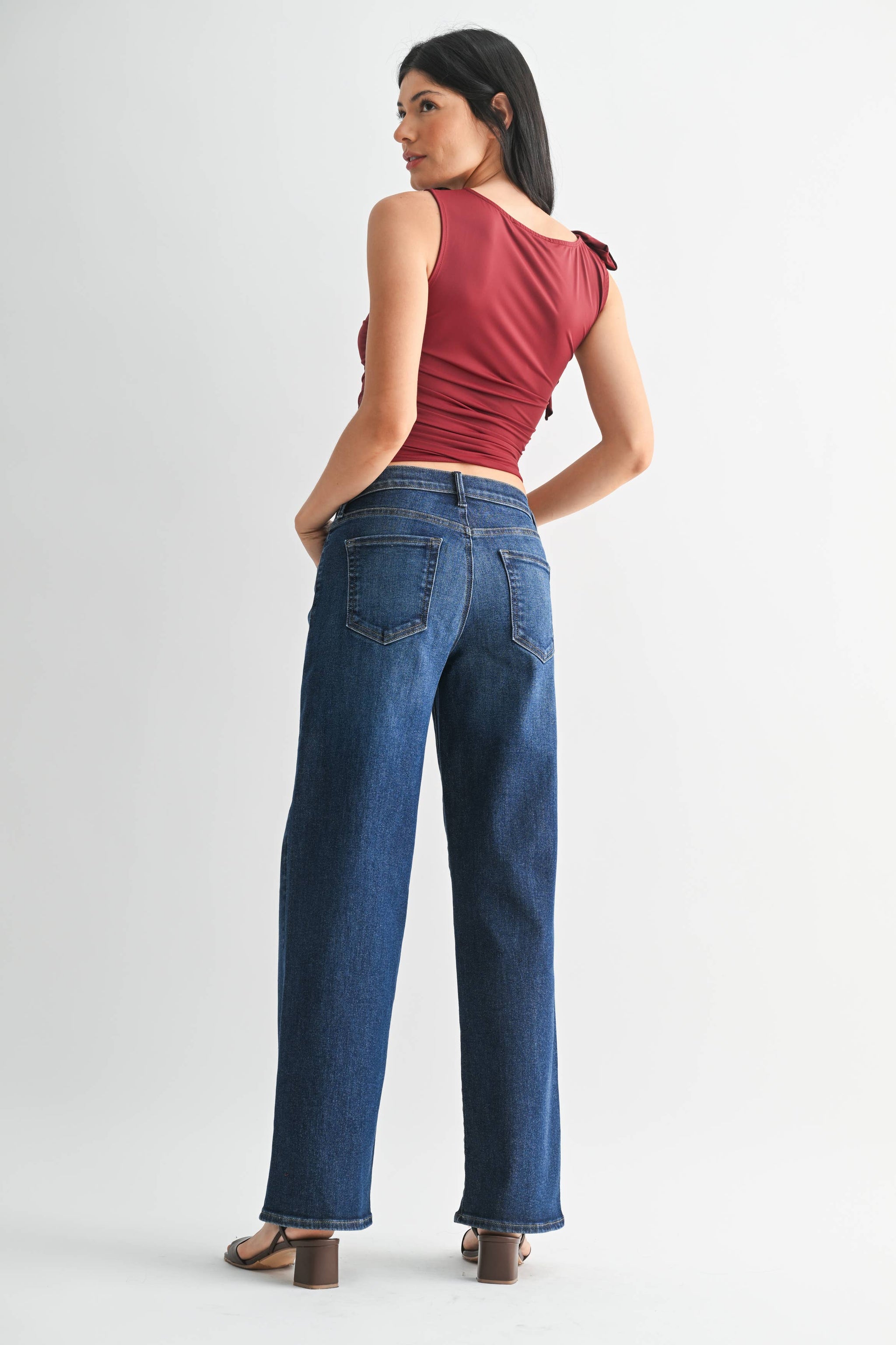 Woman wearing blue jeans and a red top on a white background showing back view.

