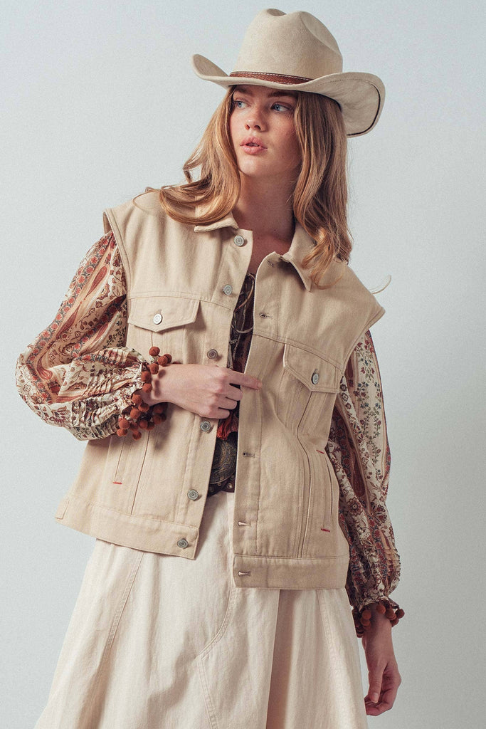 Woman wearing a beige vest, patterned blouse, and cowboy hat against a white background