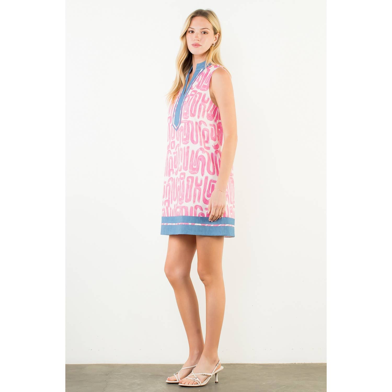 Woman wearing a pink dress with blue accents on a white background showing side view