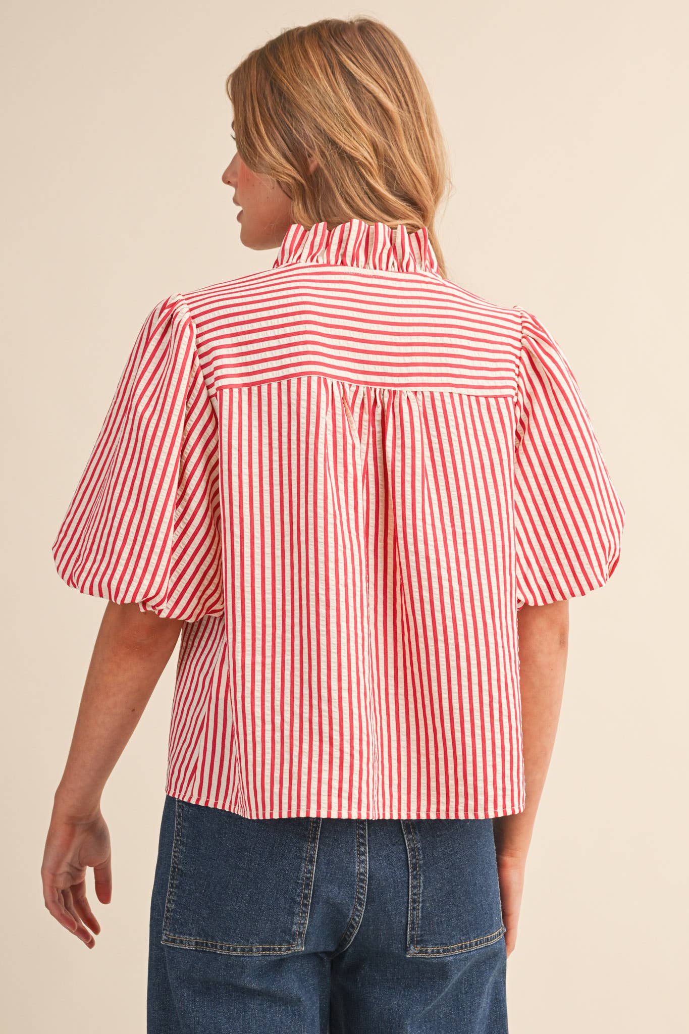 Woman wearing a red and white striped blouse with blue jeans on a beige background