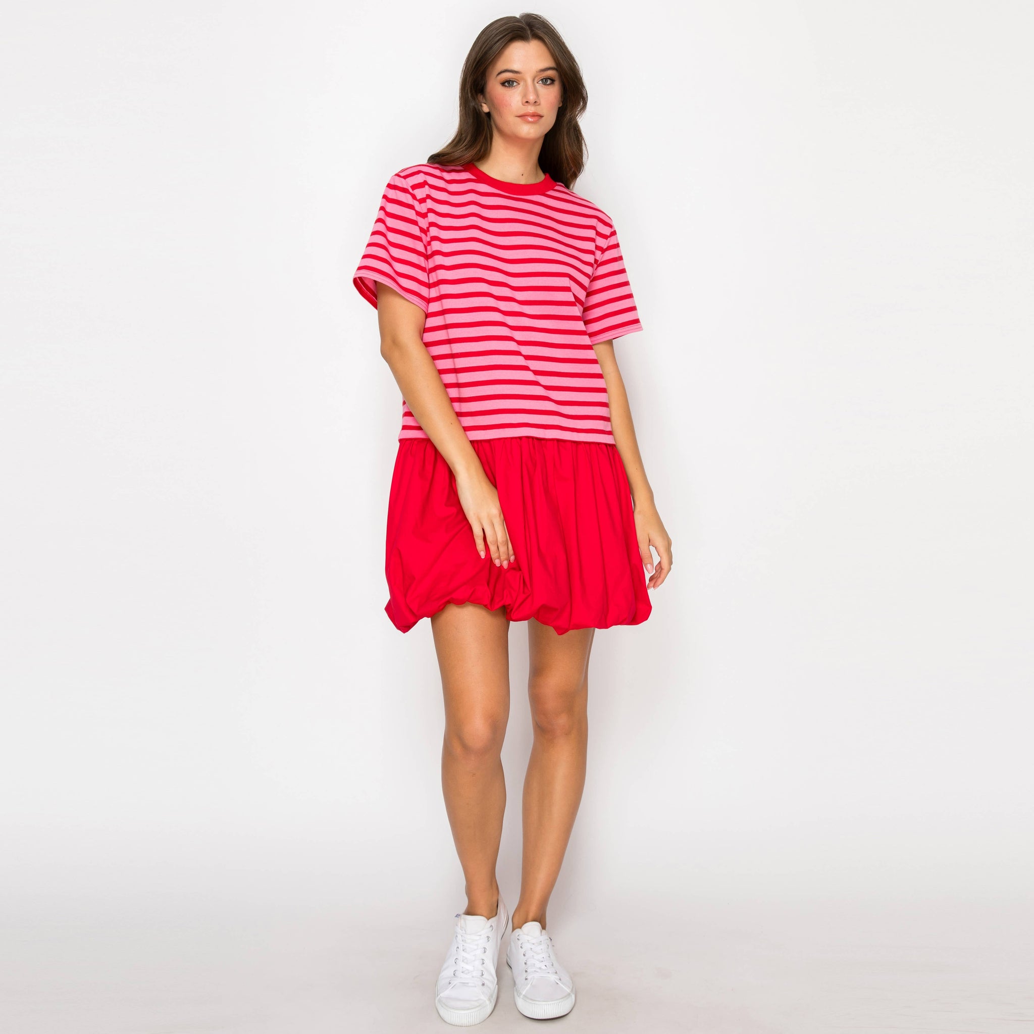 Woman wearing a red and pink striped dress with white sneakers on a white background. Front view.