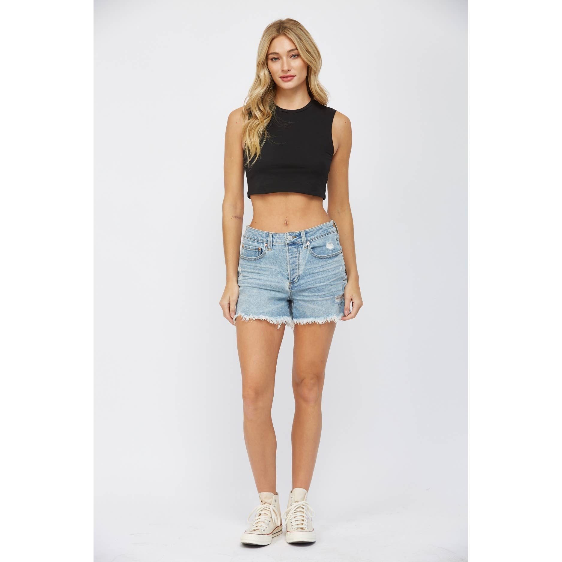 Woman wearing a black sleeveless crop top and denim shorts on a white background